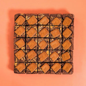 Crumbs & Doilies Biscoff Brownie squares topped with Lotus biscuits on an orange background, fudgy and rich.
